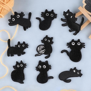 Peut inclure: Neuf patchs thermocollants en feutre noir représentant des chats noirs dans différentes poses. Les chats sont tous dans un style simple et cartoon.