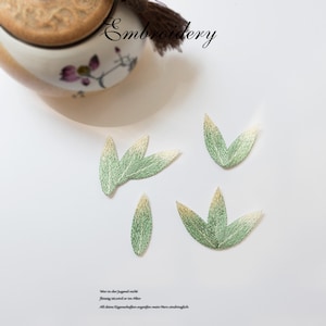 May include: Five embroidered green and white leaf shapes on a white background. The leaves are arranged in a random pattern. The word "Embroidery" is written in black at the top of the image.