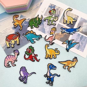 May include: A collection of colorful dinosaur patches in various shapes and sizes. The patches feature different dinosaur species in shades of green, yellow, blue, red, and purple. These embroidered patches are ideal for decorating clothing or accessories.