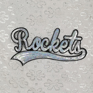Op de afbeelding: Een strijkbare patch met het woord "Rockets" in een cursief schrift, gemaakt van zilveren pailletten.
