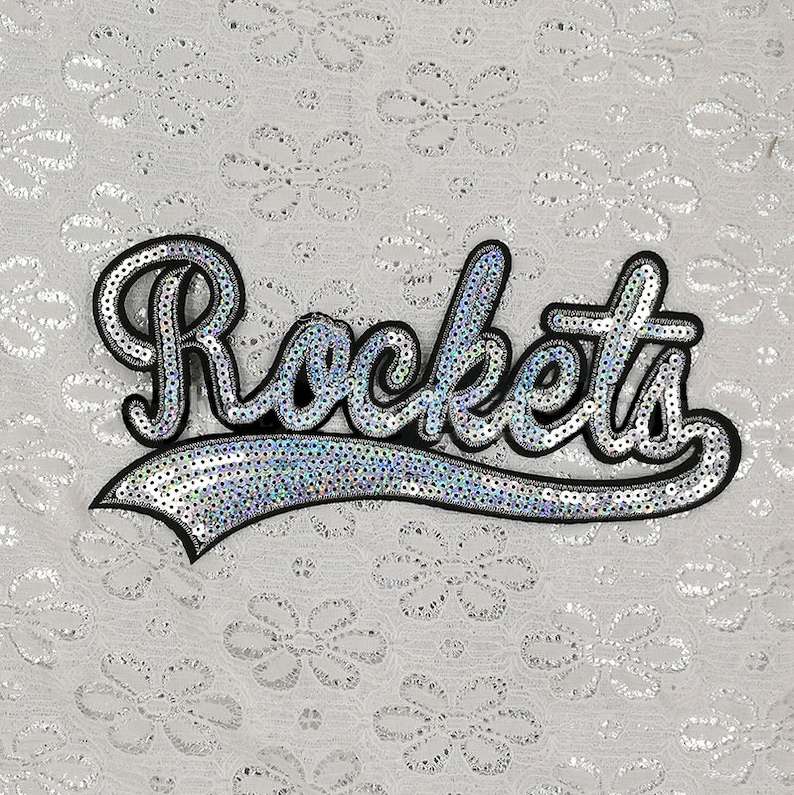 Op de afbeelding: Een strijkbare patch met het woord "Rockets" in een cursief schrift, gemaakt van zilveren pailletten.