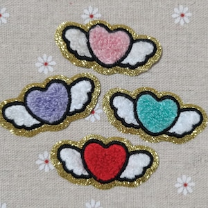 Op de afbeelding: Vier geborduurde strijkpatches met pluche harten en witte vleugels. De harten zijn roze, paars, turquoise en rood.