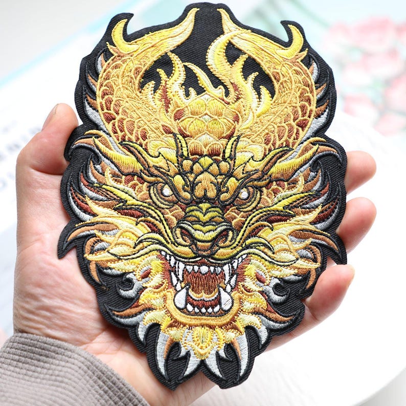 May include: Embroidered patch featuring a detailed golden dragon design on a black background. The dragon has intricate scales, sharp teeth, and a fierce expression. The patch is likely for jackets, bags, or other apparel.