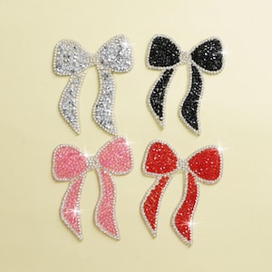 May include: Four rhinestone bows in different colors: silver, black, pink, and red. Each bow is made of small, sparkling rhinestones.