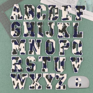Peut inclure: Un ensemble de 26 lettres en feutre blanc avec un motif camouflage dans les tons de vert et de bleu. Les lettres sont disposées en ordre alphabétique.