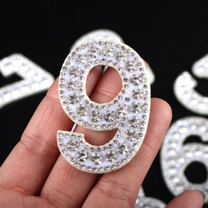 May include: A white felt number nine with clear rhinestones. The number is about 2 inches tall and is perfect for adding a touch of sparkle to any project.