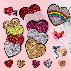 May include: Assortment of colorful heart-shaped patches with sequin embellishments. The patches feature various designs, including a rainbow, a heart with an arrow, and a double heart.