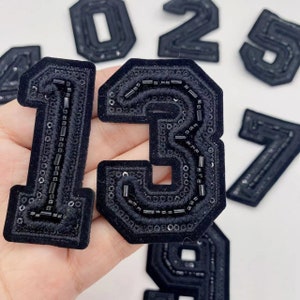 May include: Black felt fabric numbers with black bead embellishments. The numbers are 1, 2, 3, 5, 7, and 9.