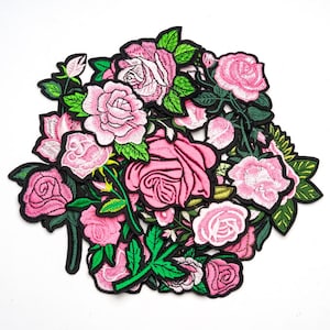 May include: A collection of embroidered rose patches in various stages of bloom. The patches feature shades of pink and green, with black outlines. The roses are arranged in a dense, overlapping pattern, creating a floral design.