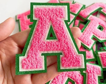 May include: Pink felt letter A with a white outline and green trim. The letter is large, puffy, and has a varsity style.