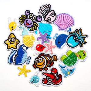 May include: A selection of embroidered patches depicting marine life. The patches include a crab, starfish, whale, octopus, clownfish, and a sea turtle. The patches are in shades of blue, yellow, red, purple, and green.