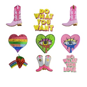 May include: A set of nine iron-on patches featuring various designs, including a rainbow heart, a green heart with an eye, a pink heart with an eye, a pair of pink cowboy boots, a pair of gray cowboy boots, a strawberry with a rainbow, and two phrases: "Do What You Want" and "Do What You Love".