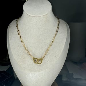 Peut inclure: Un collier en chaîne dorée avec un pendentif en forme de menottes.