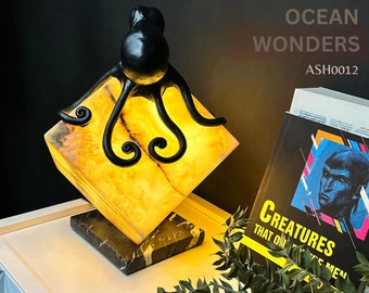 Puede incluir: Una escultura de pulpo de metal negro con tentáculos rizados se asienta sobre una base de lámpara de cubo de ónix amarillo y blanco. La lámpara está sobre una base de mármol negro. El texto "OCEAN WONDERS" y "ASH0012" es visible en el fondo.