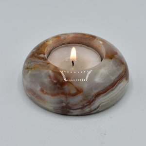 May include: A white, brown, and beige marble candle holder with a round shape and a small, white tea light candle burning inside.