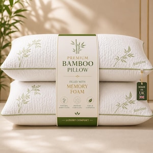 May include: Two white pillows stacked vertically, wrapped in a paper band labelled PREMIUM BAMBOO PILLOW FILLED WITH MEMORY FOAM. The pillows feature green bamboo stalk embroidery, green piping, and a tag reading MADE IN UK with a Union Jack icon.