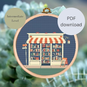 May include: A cross-stitch pattern of a bookstore with a striped awning, shelves full of books, and a sign that says "Book Nook". The pattern is in a circular hoop and is on a blue background. This is an intermediate level cross-stitch pattern.