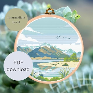 Könnte beinhalten: Ein Kreuzstichmuster einer Bergsee-Szene mit blauem Himmel, weißen Wolken und grünen Bäumen. Das Muster befindet sich in einem runden Holzstickrahmen. Der Text "PDF-Download" befindet sich auf einem blauen Kreis unten links. Der Text "Mittleres Niveau" befindet sich auf einem grünen Kreis oben links.