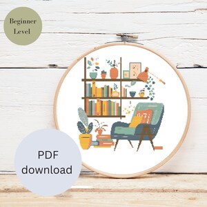May include: Cross stitch pattern of a living room with a bookshelf, armchair, and plants. The bookshelf is filled with books and has a small potted plant on top. The armchair is blue and has a yellow pillow. The plants are green and have brown pots. The pattern is in a beginner level.