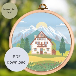 Könnte beinhalten: Kreuzstichmuster mit einem weißen Haus mit braunem Dach und grünen Bäumen vor einer Bergkette. Der Himmel ist blau mit weißen Wolken und einer gelben Sonne. Das Muster ist mit "Mittleres Niveau" und "PDF-Download" gekennzeichnet.