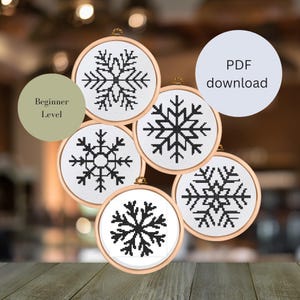 Könnte beinhalten: Fünf schwarze und weiße Schneeflocken-Kreuzstichmuster in Stickrahmen. Die Muster sind für Anfänger geeignet und als PDF-Download verfügbar.