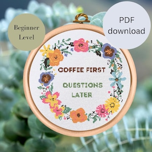 Könnte beinhalten: Ein Kreuzstich-Muster für Anfänger mit einem Blumenkranz und dem Text "Coffee First Questions Later".