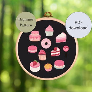 Könnte beinhalten: Ein schwarz-weißes Kreuzstichmuster mit verschiedenen rosa Desserts, darunter Cupcakes, Tortenstücke, Donuts und Macarons. Das Muster ist in einem Holzreifen gerahmt und mit "Anfängermuster" beschriftet.