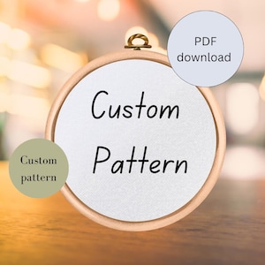Könnte beinhalten: Ein weißer Stickrahmen mit dem Text "Custom Pattern" in Schwarz. Der Rahmen liegt auf einer Holzoberfläche. Im Hintergrund ist ein PDF-Download-Button zu sehen.