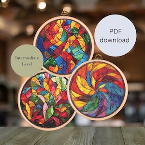 Könnte beinhalten: Drei bunte Stickrahmen-Kunstwerke mit Buntglas-Designs. Die Designs sind abstrakt und zeigen eine Vielzahl von Farben, darunter Rot, Gelb, Blau, Grün und Lila. Die Rahmen sind aus Holz und haben eine natürliche Oberfläche. Der Text "Mittleres Niveau" ist im Bild sichtbar.