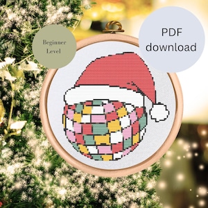 Könnte beinhalten: Ein Kreuzstichmuster einer bunten Discokugel, die einen roten Weihnachtsmann-Hut trägt. Das Muster ist in einem Holzreifen gerahmt und mit "Anfänger-Level" beschriftet.