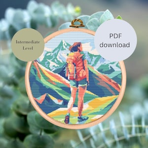 May include: Cross stitch pattern of a person hiking in the mountains. The pattern is in a round hoop and is labeled "Intermediate Level".