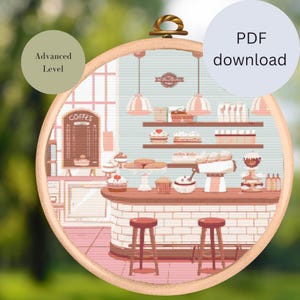 Könnte beinhalten: Kreuzstichmuster eines Bäckereieinrichtungs mit einer Theke, Regalen mit Gebäck und zwei Hockern. Das Muster ist in einem Pastellfarbschema mit rosa, blauen und braunen Tönen gehalten. Der Text "COFFEE" ist auf einem Schild sichtbar.