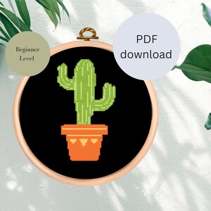 Könnte beinhalten: Ein Kreuzstichmuster eines grünen Kaktus in einem orangefarbenen Topf auf schwarzem Hintergrund. Das Muster ist mit "Anfänger-Level" gekennzeichnet und beinhaltet einen PDF-Download.