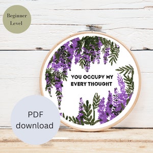 Könnte beinhalten: Ein Kreuzstichmuster mit einem floralen Design mit lila Blüten und grünen Blättern. Das Muster enthält den Text "You occupy my every thought".