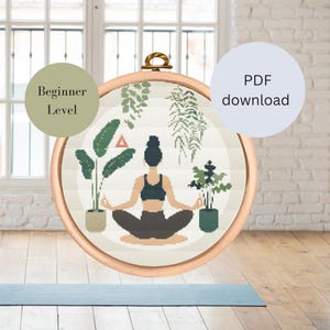 Puede incluir: Un patrón de punto de cruz con una mujer meditando en una postura de yoga rodeada de plantas. El patrón está etiquetado como "Nivel principiante" y está disponible para descargar en PDF.