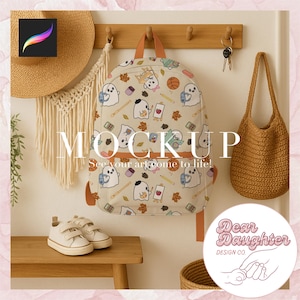 Puede incluir: Una mochila beige con un estampado de fantasmas de dibujos animados, lápices y hojas cuelga de un perchero de madera. La mochila tiene correas naranjas. La palabra "MOCKUP" se muestra en la pared, junto con el texto "See your art come to life!"