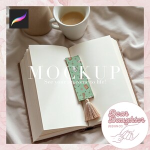 Può includere: Un segnalibro verde a fantasia con un nappa beige è inserito in un libro aperto. Il segnalibro presenta piccole illustrazioni e il testo "MOCKUP See your art come to life!" Sono visibili anche una tazza di caffè e un logo.