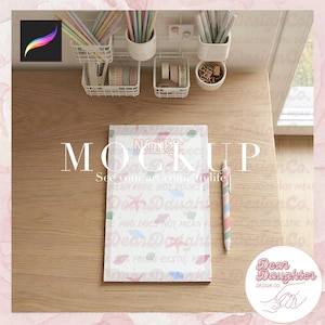 May include: A mockup of a notepad with the text "MOCKUP" and "See your art come to life!" on a wooden desk. A pen with pastel stripes and various stationery items are also visible. The notepad has the text "Dear Daughter" and other text.