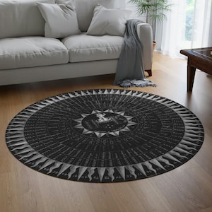 May include: Black and white round rug with a circular design featuring a compass with numbers and words around the edge. The center of the rug has a starburst design with a figure in the middle.