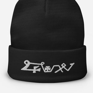 May include: Black beanie with a folded brim. The beanie features white embroidered symbols across the front. The hat is made of a soft, knitted material, suitable for cold weather. The design is simple and modern.