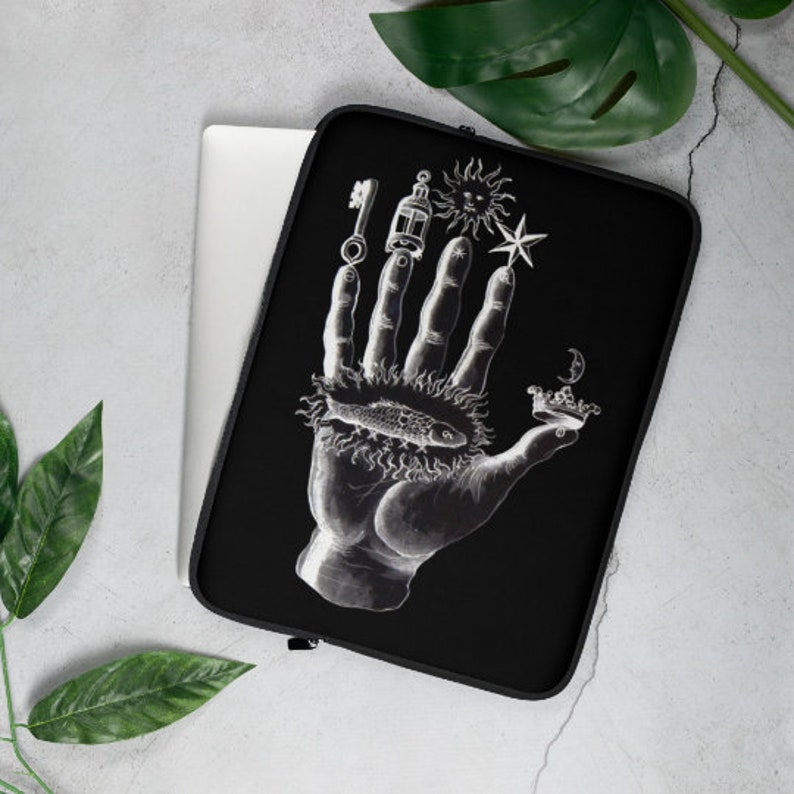 Puede incluir: Funda para port&aacute;til negra con una ilustraci&oacute;n blanca de una mano con varios s&iacute;mbolos, incluyendo una llave, una linterna, un sol, una estrella, un pez y una corona.