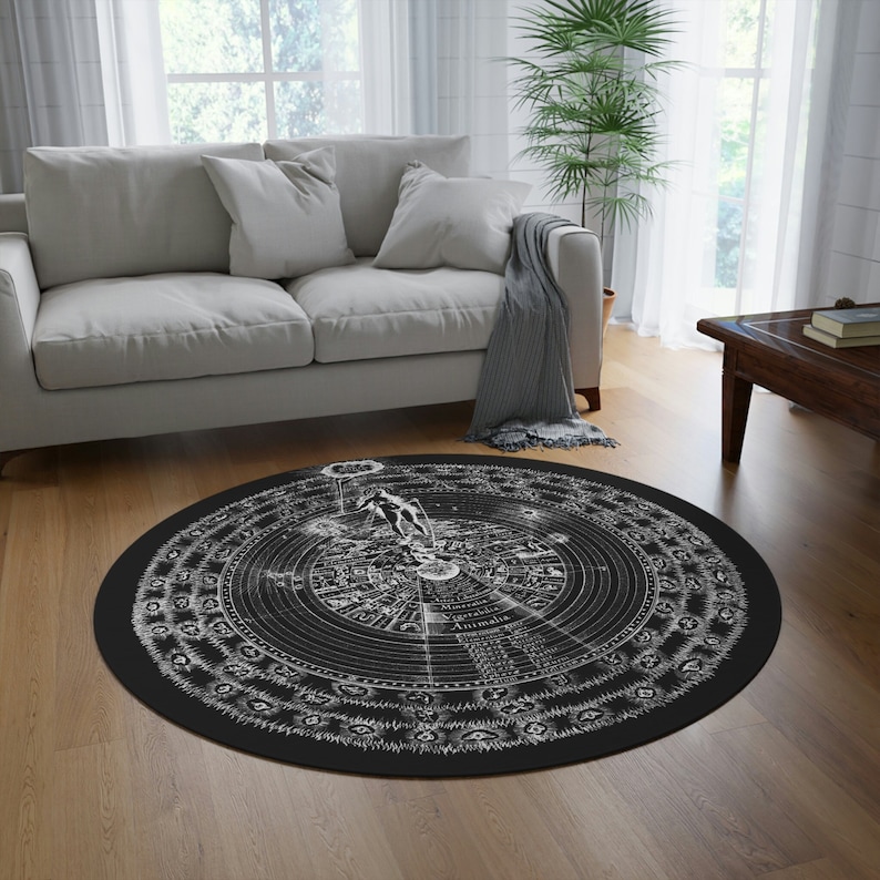 Puede incluir: Una alfombra redonda en blanco y negro con un dise&ntilde;o circular que presenta una figura humana estilizada, cuerpos celestes y texto. El dise&ntilde;o recuerda a un antiguo mapa astron&oacute;mico.