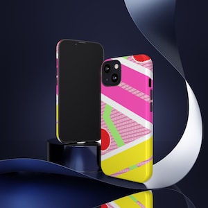 Puede incluir: Una funda de teléfono negra con un diseño geométrico colorido. La funda presenta rayas rosas, amarillas, verdes y blancas y un círculo rojo con un punto blanco.