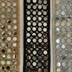May include: Close-up of three decorative trims with circular mirror accents. The trims are gold, black, and silver, each with a different border design. The gold trim has a woven edge, the black trim has a mesh design, and the silver trim has a scalloped edge.