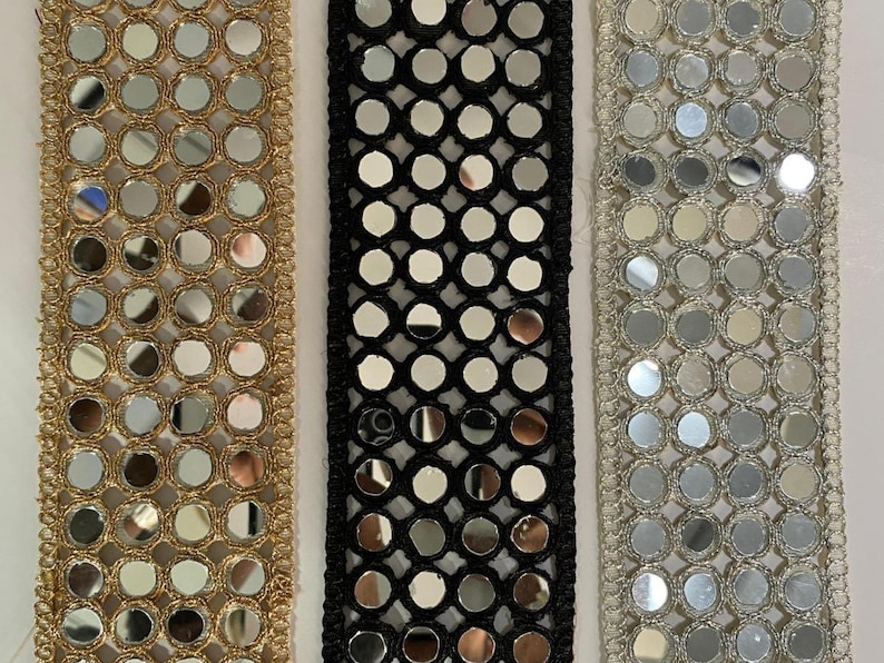 May include: Close-up of three decorative trims with circular mirror accents. The trims are gold, black, and silver, each with a different border design. The gold trim has a woven edge, the black trim has a mesh design, and the silver trim has a scalloped edge.