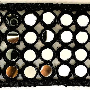 May include: Black trim with circular mirrored accents. The trim features small, round mirrors set within a black, open-weave fabric. The mirrors reflect light, creating a shimmering effect. This trim is suitable for various craft and design projects.