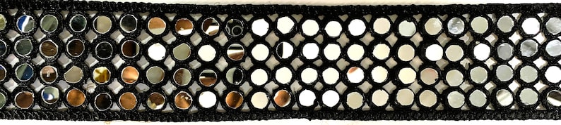 May include: Black trim with circular mirrored accents. The trim features small, round mirrors set within a black, open-weave fabric. The mirrors reflect light, creating a shimmering effect. This trim is suitable for various craft and design projects.