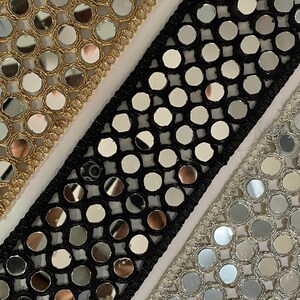 May include: Close-up of three decorative trims with reflective mirror-like embellishments. The trims are in gold, black, and silver, each with a different border design. The gold trim is on the left, the black trim is in the center, and the silver trim is on the right.