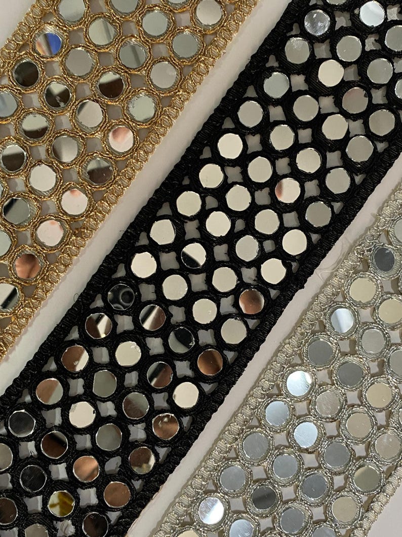 May include: Close-up of three decorative trims with reflective mirror-like embellishments. The trims are in gold, black, and silver, each with a different border design. The gold trim is on the left, the black trim is in the center, and the silver trim is on the right.