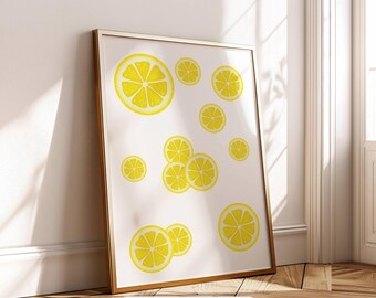 May include: A framed print featuring a white background with scattered yellow lemon slices. The artwork is in a gold frame and leans against a wall. The text "Digital Download" is at the bottom of the frame.